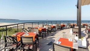 An outdoor dining area with tables and chairs, overlooking a beach and the sea. - RIU Helios Bay – All Inclusive (Obzor)