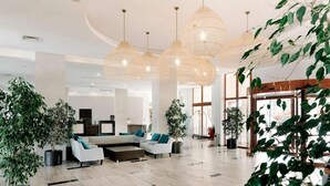 A spacious lobby with modern furniture, large hanging light fixtures, and potted plants. - RIU Helios Bay – All Inclusive (Obzor)