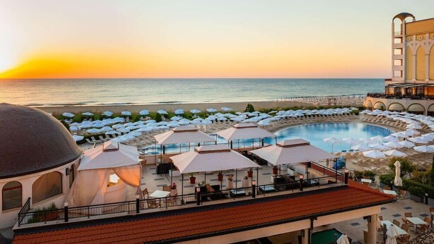 A resort with a pool, beach umbrellas, and a view of the ocean at sunset. - RIU Helios Bay – All Inclusive (Obzor)