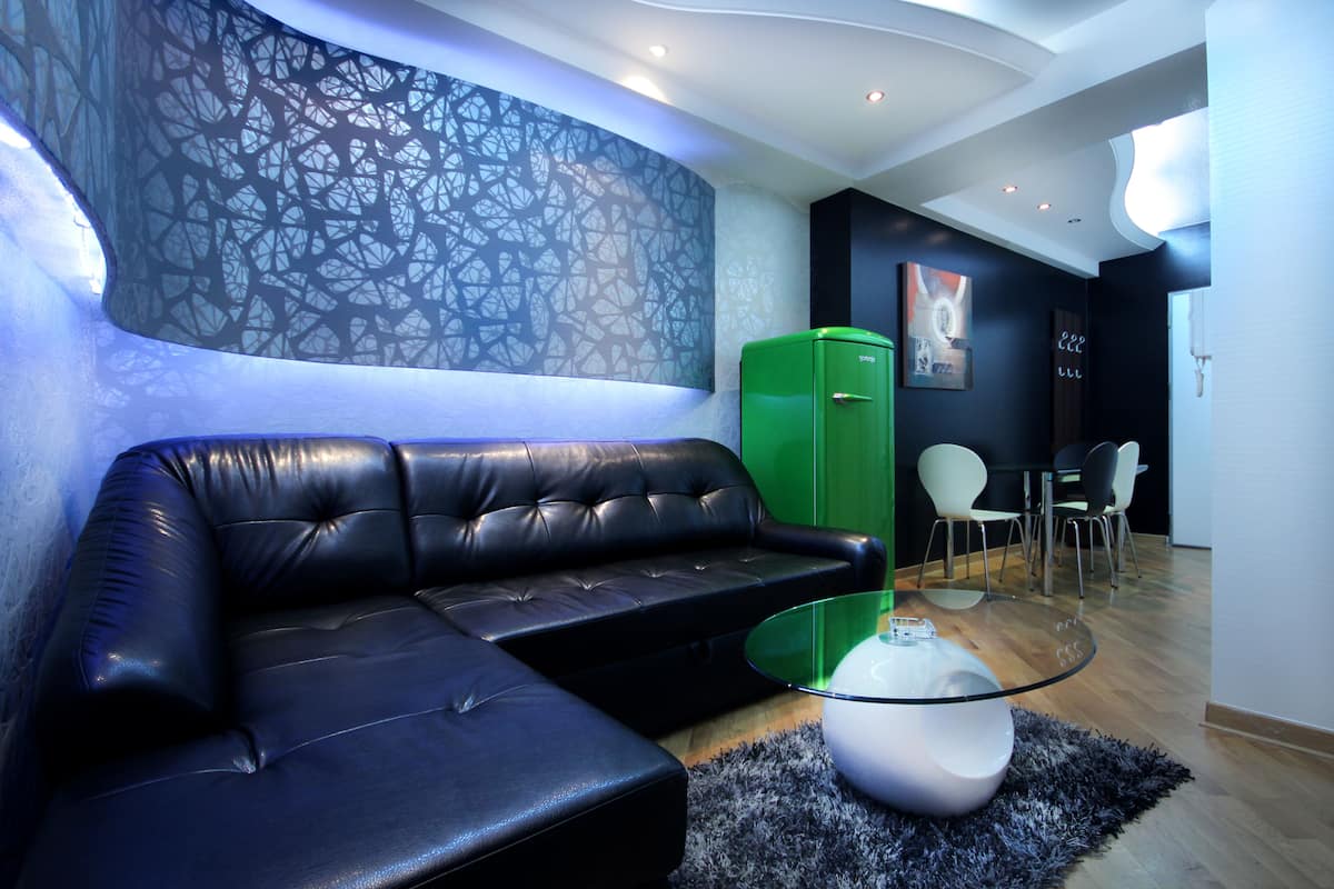 Una sala de estar moderna con un sofá de cuero negro, una mesa de centro de vidrio y un armario verde.