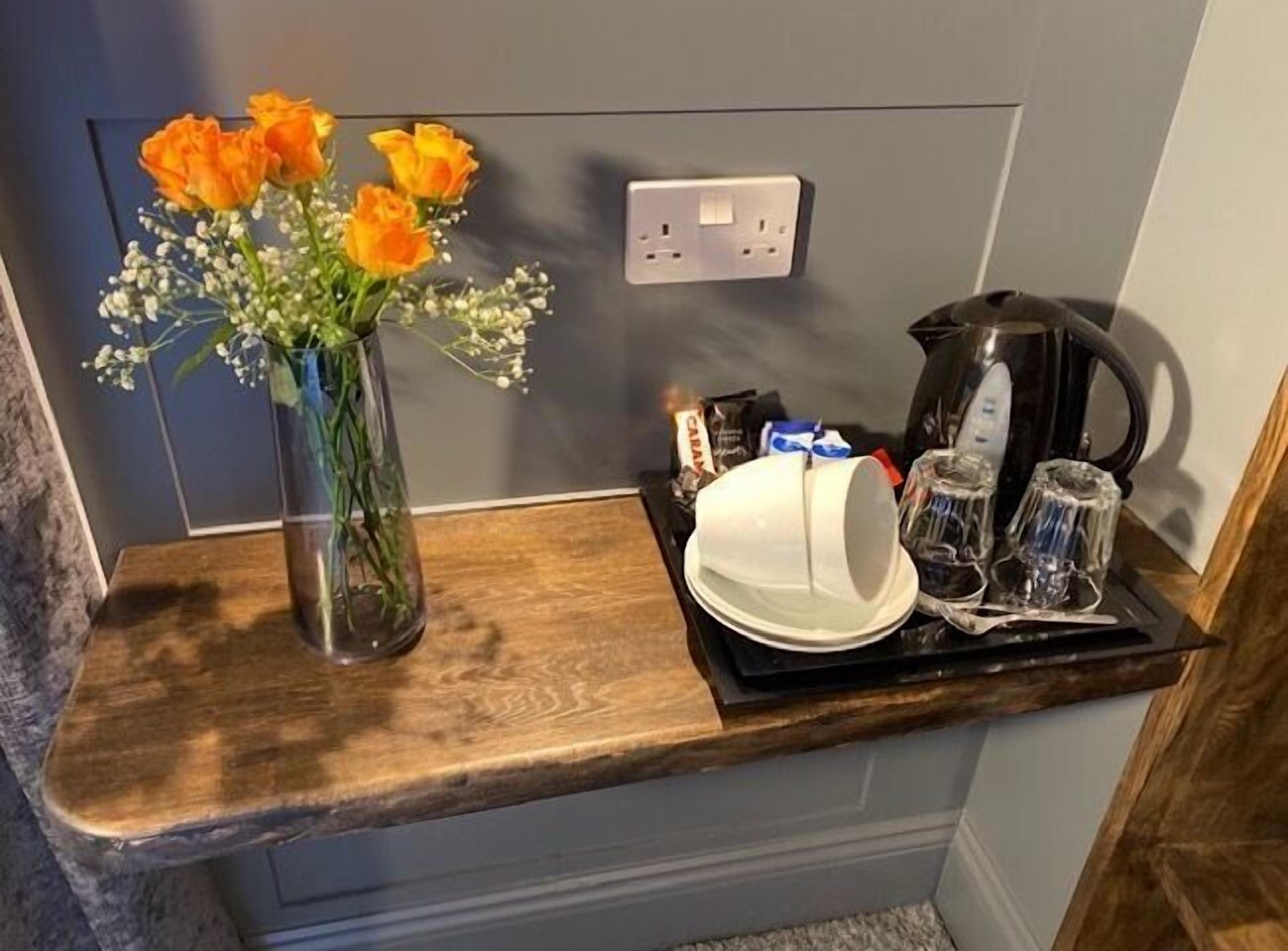 A kitchen counter with a vase of flowers, a coffee maker, and a tray with a plate and glasses.