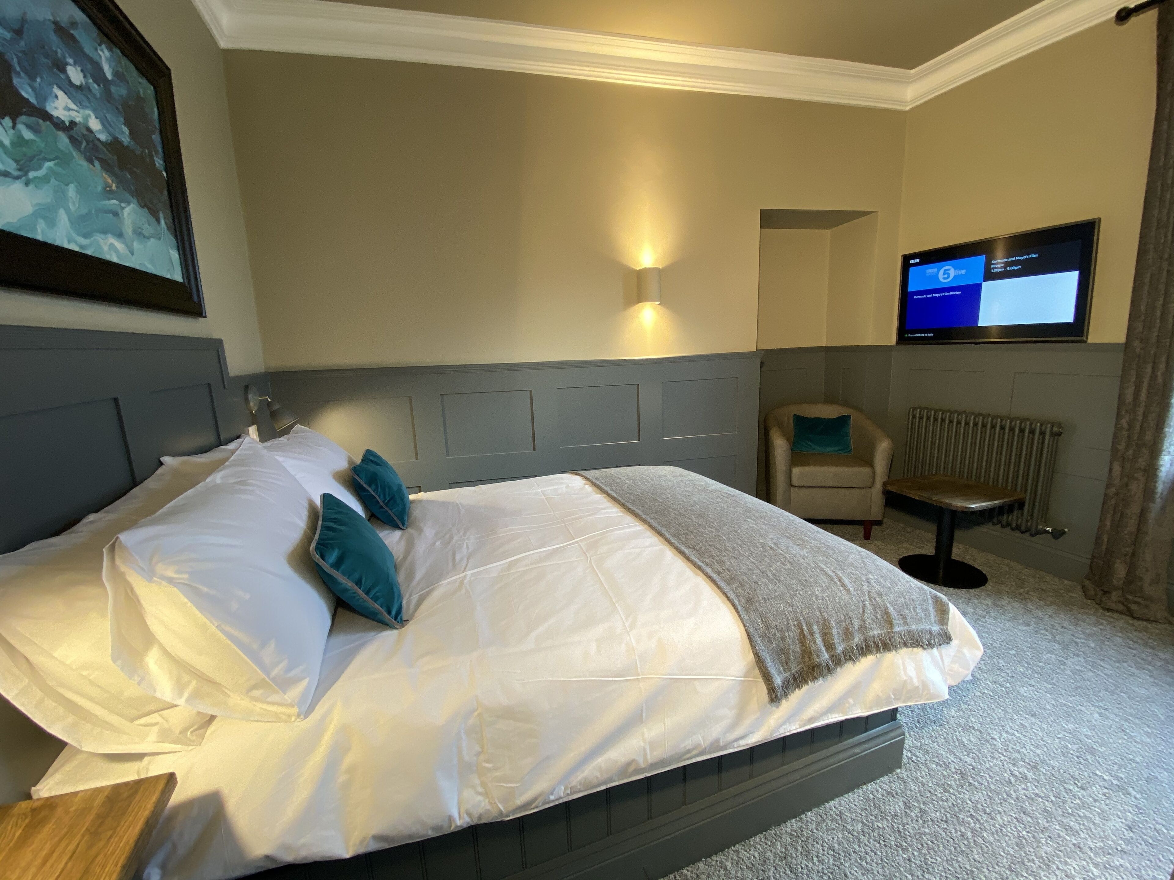 A hotel room with a large bed, a TV mounted on the wall, a chair, and a radiator.