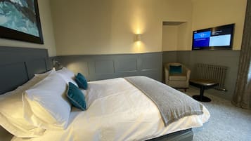 A hotel room with a large bed, a TV mounted on the wall, a chair, and a radiator.