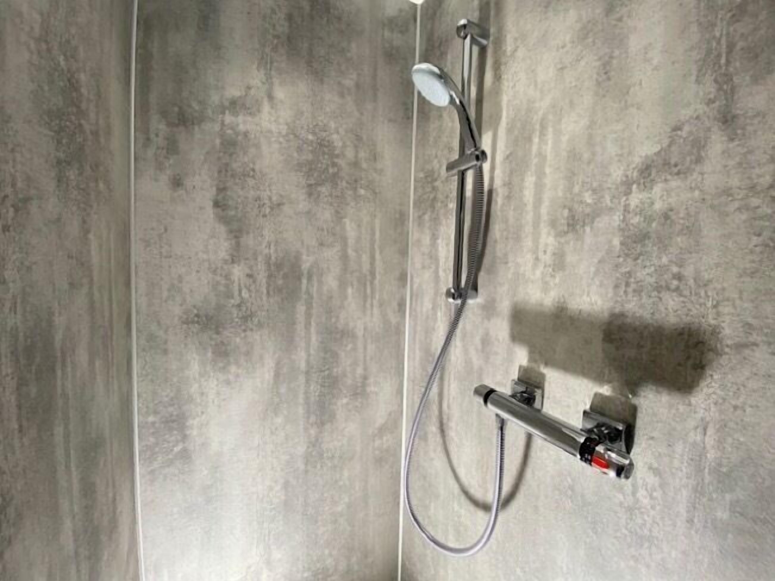 A modern shower with a handheld showerhead and a fixed showerhead, mounted on a wall with a concrete texture.