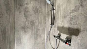 A modern shower with a handheld showerhead and a fixed showerhead, mounted on a wall with a concrete texture.