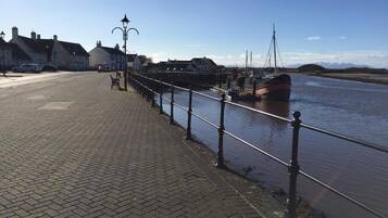 A waterfront promenade with a brick pathway, a railing, and a boat docked on the water.