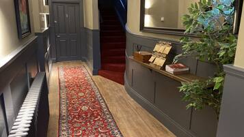 Un pasillo con alfombra roja estampada, un banco de madera, un radiador, una escalera y una planta.