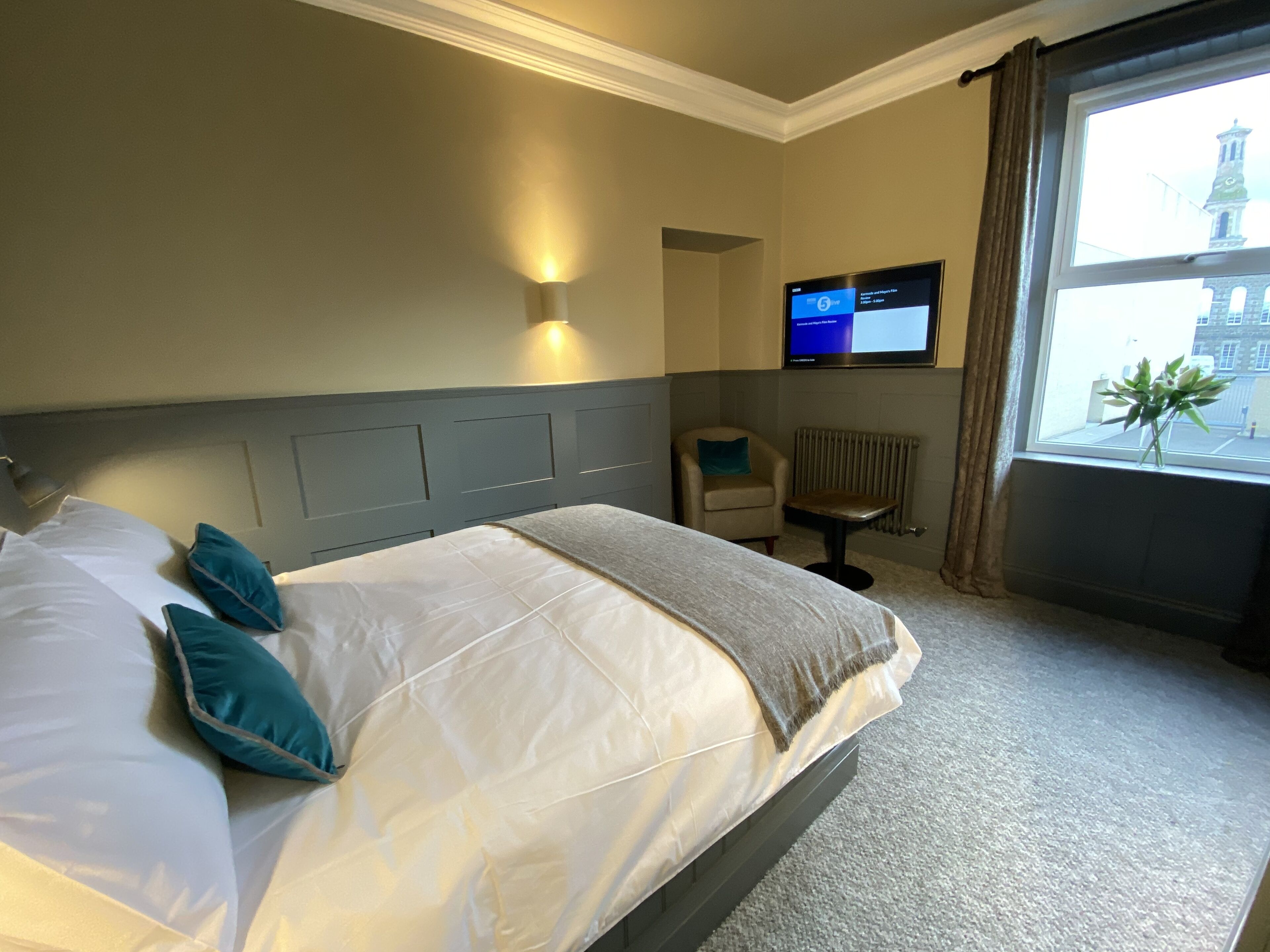 A hotel room with a bed, a chair, a TV, and a window with a view of a building.