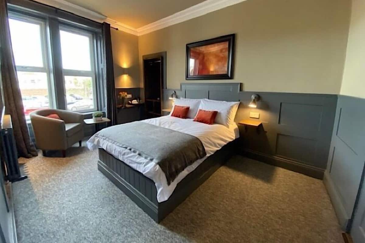 A hotel room with a large bed, bedside lamps, a chair, a desk, and a window with curtains.