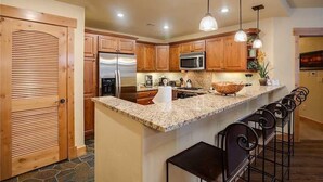 Une cuisine moderne avec des meubles en bois, des appareils en acier inoxydable, un plan de travail en granit et des luminaires suspendus.