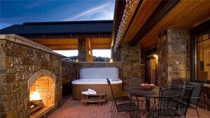 Une cheminée en pierre, un jacuzzi et un espace extérieur aménagé avec vue sur le ciel.