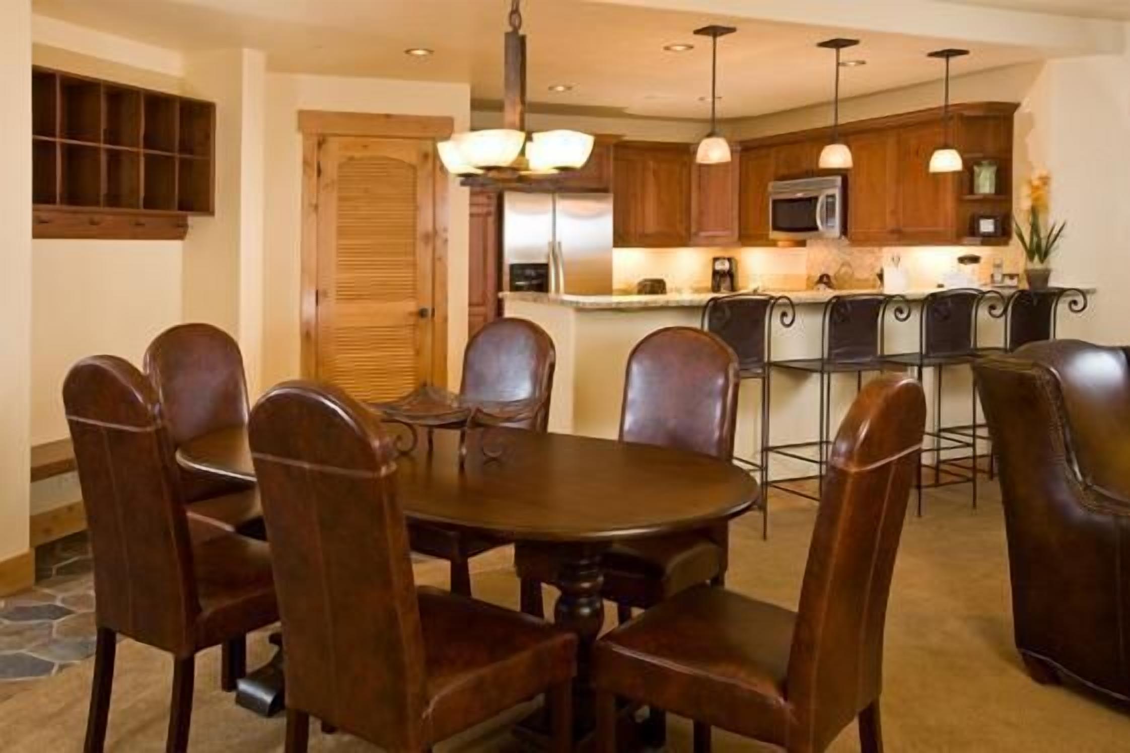A dining area with a round table and six chairs, a kitchen with wooden cabinets and stainless steel appliances, and a bar area with stools.