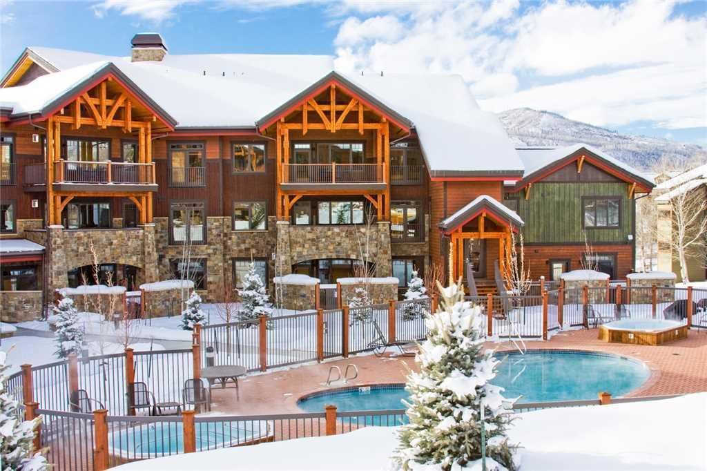 A multi-story lodge with a pool and outdoor seating, surrounded by snow.
