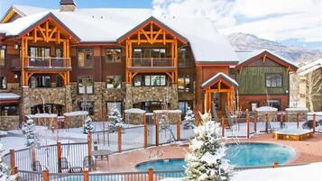 A multi-story lodge with a pool and outdoor seating, surrounded by snow.