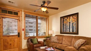 A living room with a brown leather sofa, a wooden coffee table, and a ceiling fan. - 6115 Bear Lodge, Trappeur's Crossing Apartment 1 (Steamboat Springs)