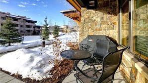 An outdoor patio with a stone wall, a grill, and a table with chairs. - 6115 Bear Lodge, Trappeur's Crossing Apartment 1 (Steamboat Springs)