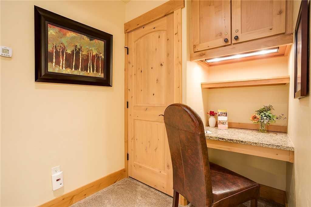 Une petite pièce accueillante, avec une porte en bois, un tableau encadré au mur, un bureau avec une chaise et une étagère ornée d’un vase de fleurs.