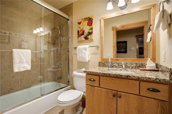 Un bagno con doccia vetro, water, lavabo con piano in granito, mobili in legno e uno specchio grande.