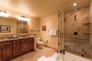 Een badkamer met een douche met glazen wand, een houten wastafelmeubel, een grote spiegel en een bad.