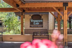 Een houten pergola constructie met een bord waarop staat: "Trappeur's Lair CHECK-IN OFFICE" voor een gebouw.