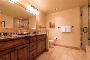 A bathroom with a wooden vanity, a large mirror, a glass shower enclosure, and a toilet.