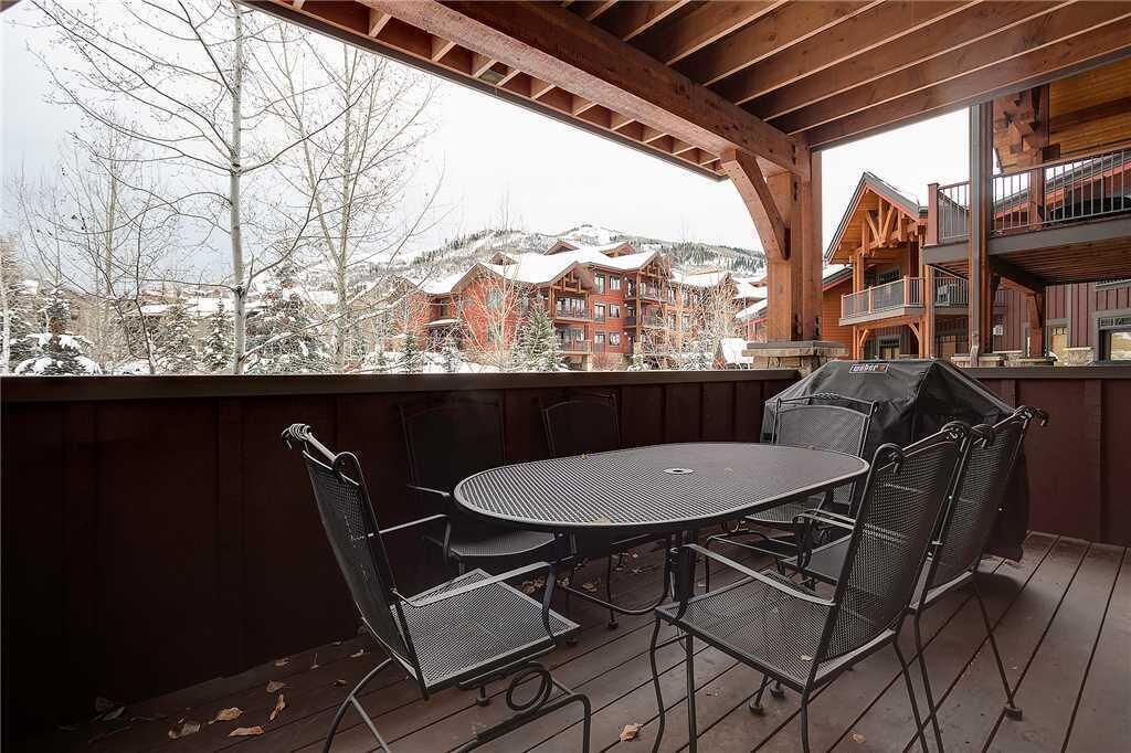 Une terrasse extérieure couverte, avec une table ronde et des chaises, d’où l’on peut admirer une montagne enneigée et des bâtiments.
