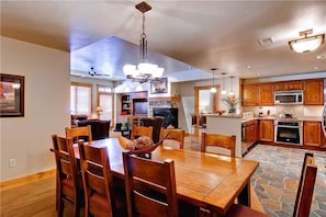 A spacious dining area with a wooden table and chairs, a chandelier, and a stone-tiled floor. - 6209 Bear Lodge, Trappeur's Crossing Apartment 3 (Steamboat Springs)
