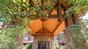 Une entrée couverte en bois, soutenue par des piliers en pierre, une façade en pierre et une vue dégagée sur l’entrée du bâtiment.