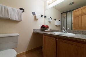 Ein Badezimmer mit Toilette, Waschbecken, Holzsärchen, einem Spiegel und Handtüchern an einem Handtuchhalter.
