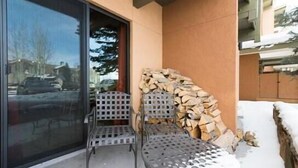 A patio with metal chairs and a table, a stack of firewood, and a glass door leading to a snowy street. - 218 Storm Meadows Club B Apartment 1 (Steamboat Springs)