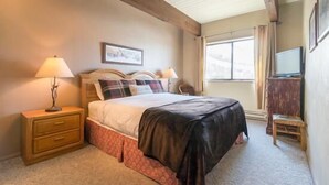 Un dormitorio con cama, mesita de noche, lámpara y ventana con cortinas.