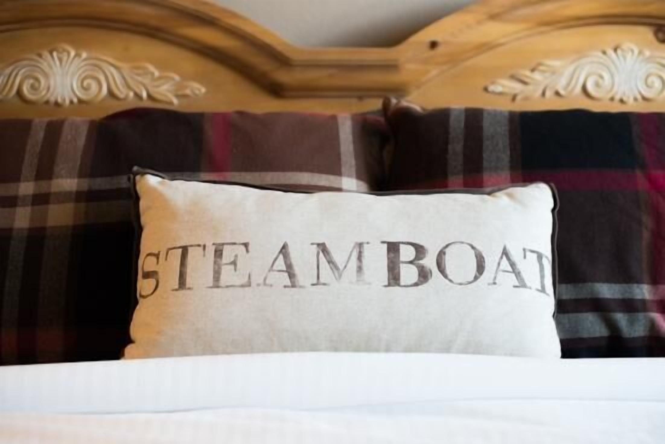 Un lit avec une couverture à carreaux et un oreiller orné du mot « STEAMBOAT ».