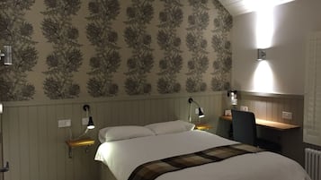 A bedroom with a bed, bedside tables, lamps, a desk, and a radiator.