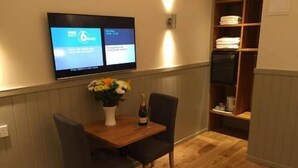 Una habitación con una mesa de madera, dos sillas, un florero con flores, una botella y un televisor montado en la pared mostrando un menú de servicio a la habitación.