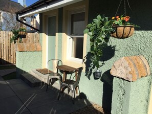 A patio with two metal chairs, a small table, and hanging planters with flowers. - Irvine Bay Studios (Irvine)
