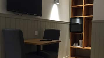A dining area with a wooden table and two chairs, a television mounted on the wall, and a built-in shelving unit with a TV and some items on the lower shelf.