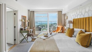 A hotel room with a large bed, a desk with a chair, a view of the sea, and a balcony with a table and chairs. - Thurlestone Hotel (Kingsbridge)