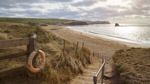 A beach with a wooden fence, a lifebuoy, and a staircase leading down to the shore. - Thurlestone Hotel (Kingsbridge)
