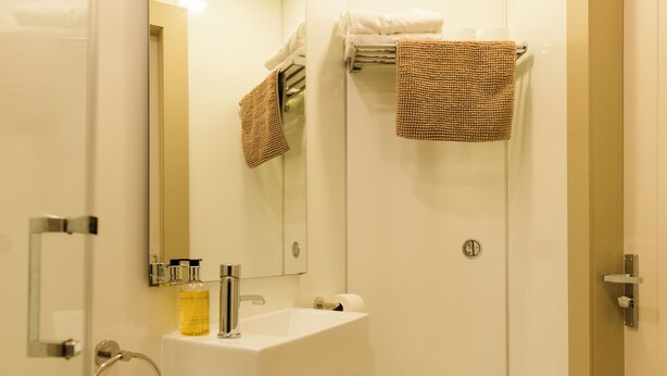 Un baño con lavamanos, espejo, toallero y retrete.