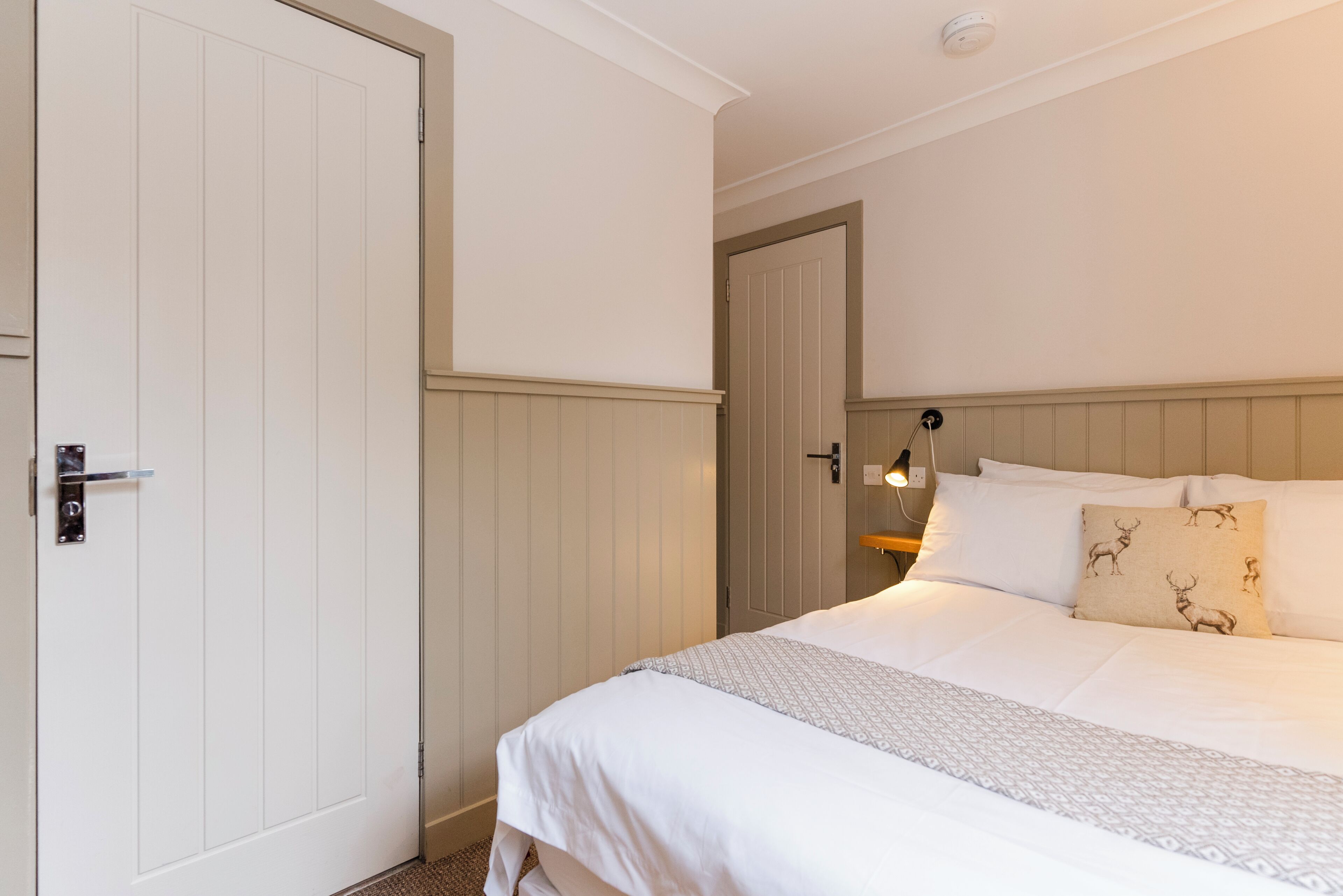 A bedroom with a bed, a door, and a nightstand with a lamp.