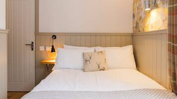 Una habitación de hotel con una cama, una mesita de noche, una lámpara y una puerta.