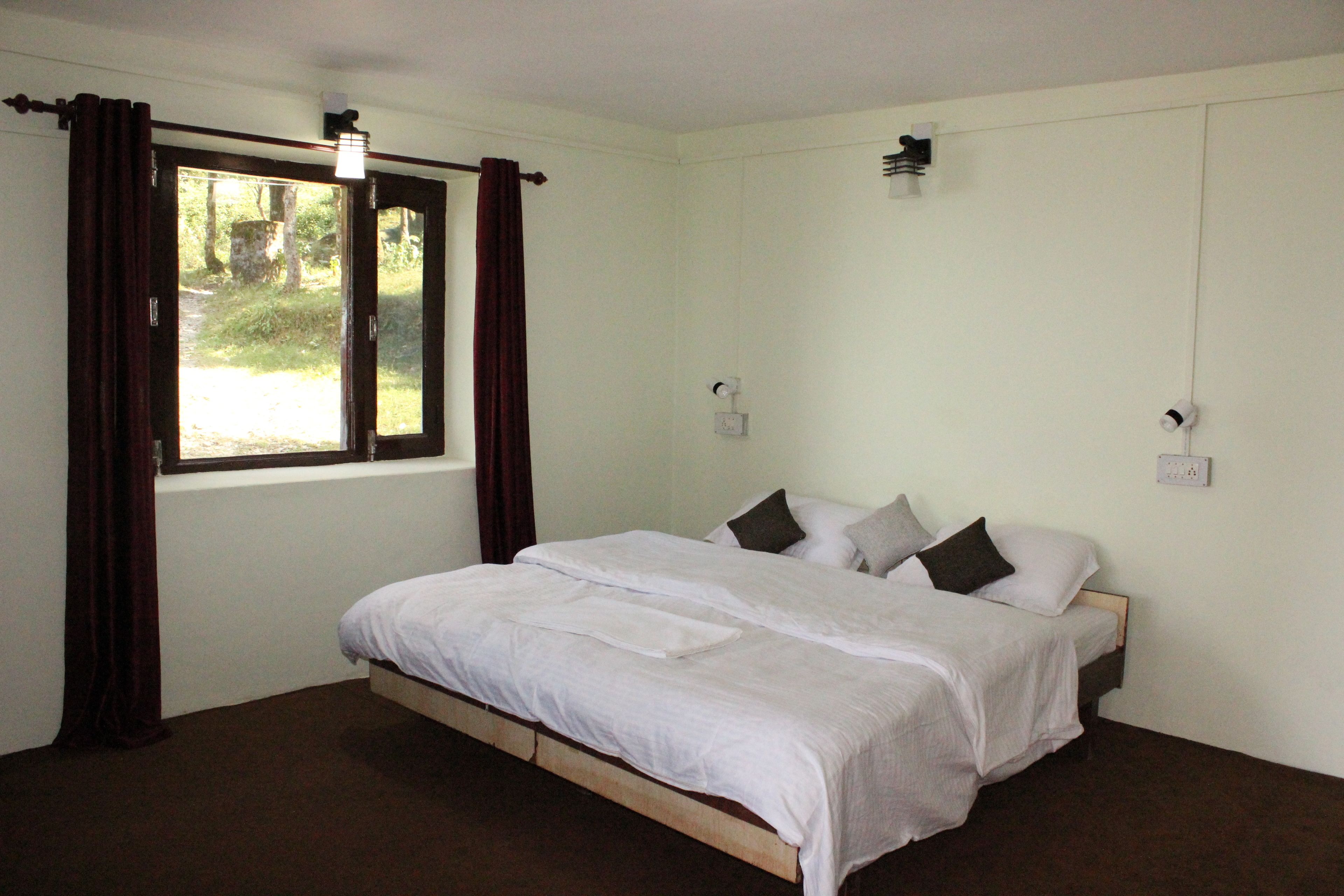 A bedroom with a single bed, white bedding, a window with curtains, and a view of greenery outside.