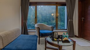 A room with a sofa, a chair, a table with a kettle, bottles, and a tray. - Treebo Regency - Bund Garden, Dhole Patil Road (Pune)