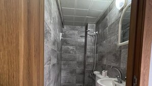 A bathroom with a shower, toilet, and sink, tiled with large gray tiles. - Gurleyen Apart Otel (Izmir)