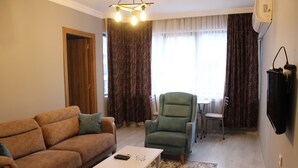 A living room with a sofa, a green armchair, a small table, and a TV. - Gurleyen Apart Otel (Izmir)