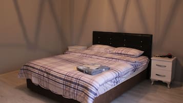A neatly made bed with a plaid bedspread and pillows, a bedside table with a lamp, and a nightstand with a phone charger.