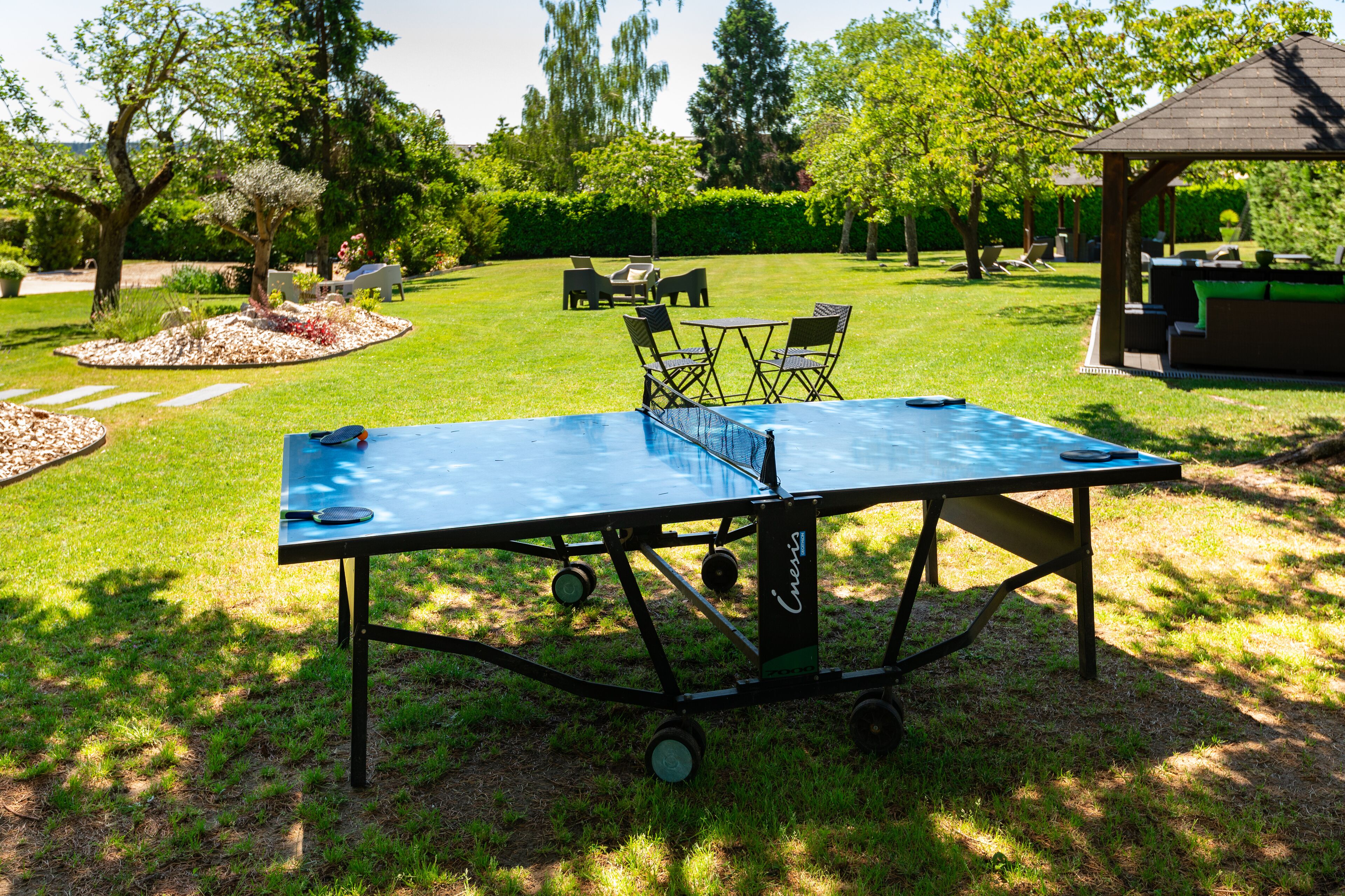 A ping pong table in a grassy outdoor area with a gazebo and lounge chairs in the background.