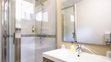 A modern bathroom with a glass-enclosed shower, a white sink with a mirror, and wooden cabinetry.