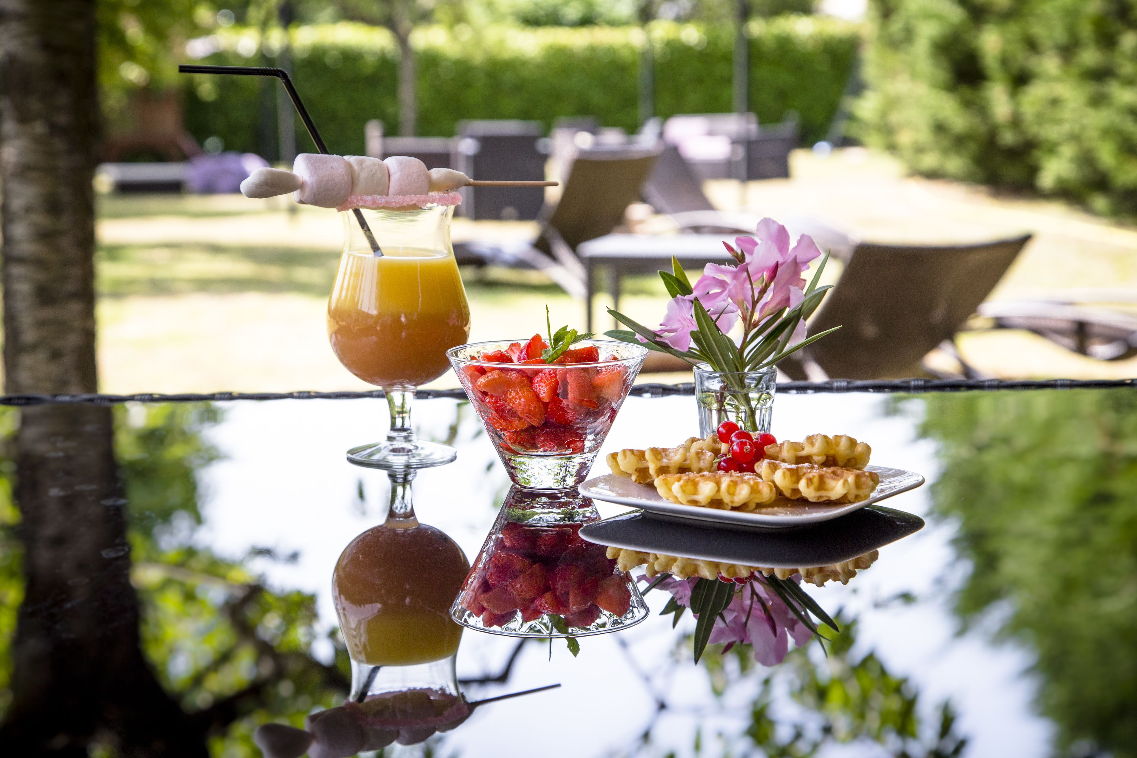Une table en verre avec une boisson, un saladier de fruits et une assiette de gaufres.