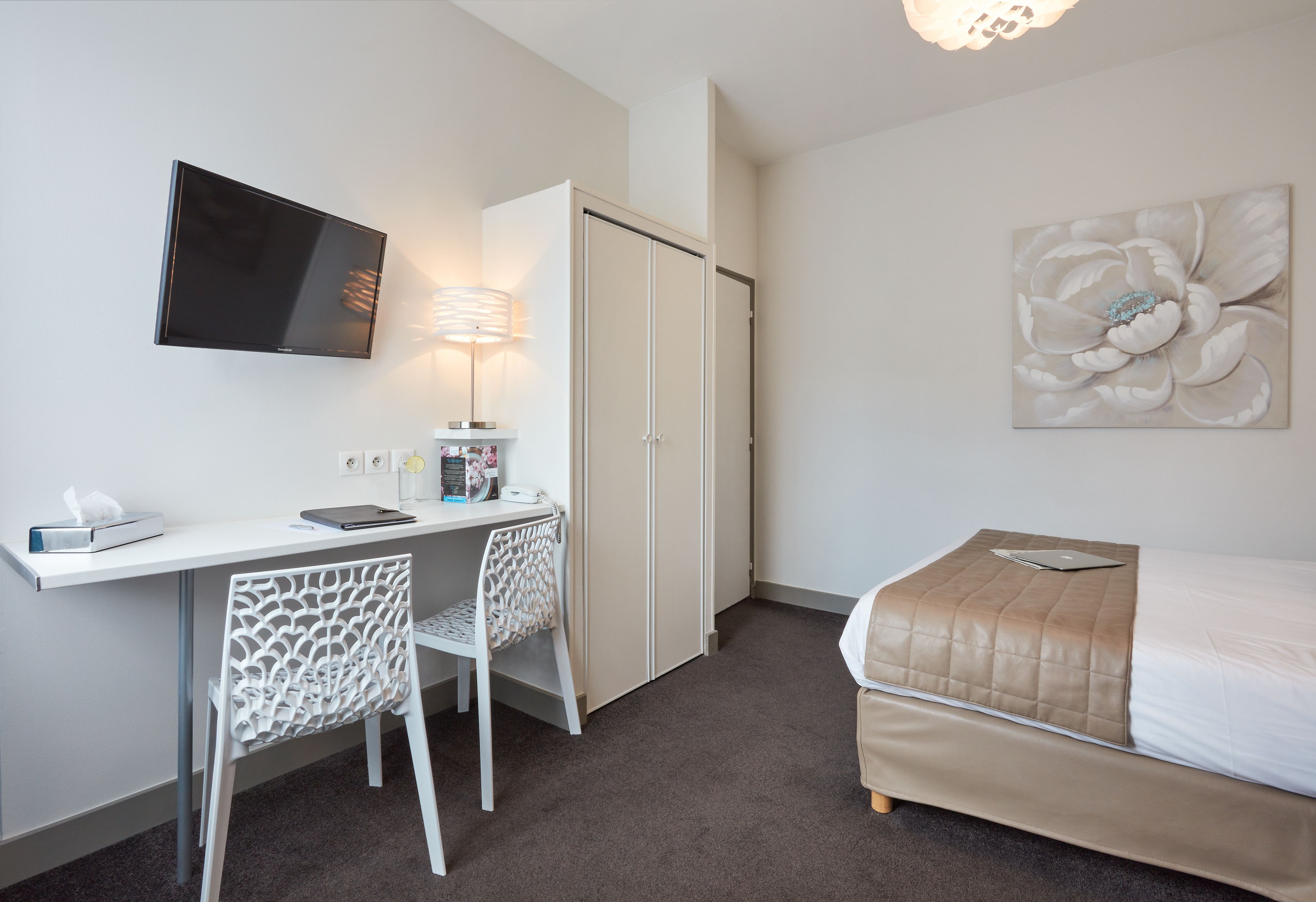 A bedroom with a bed, a desk with a chair, a TV, and a wardrobe.